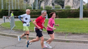 Ana-Maria Faucon en pleine course, devant un homme en tee-shirt rouge et un autre en tee-shirt blanc. Elle sourit au photographe.