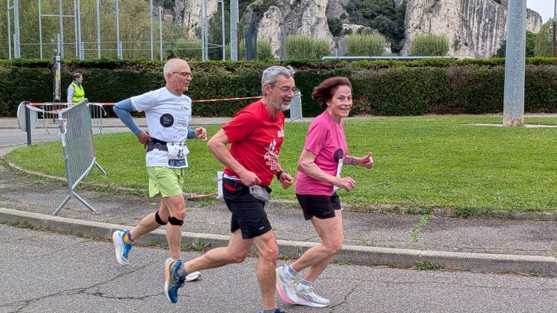 Ana-Maria Faucon en pleine course, devant un homme en tee-shirt rouge et un autre en tee-shirt blanc. Elle sourit au photographe.