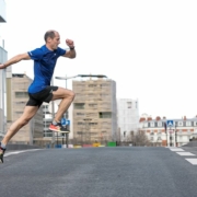 Homme en tee-shirt bleu traversant une route en simulant un saut en course.
