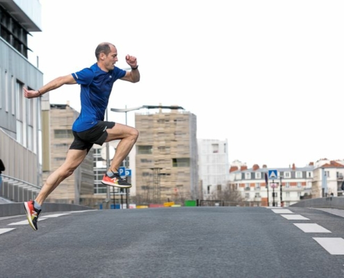 Homme en tee-shirt bleu traversant une route en simulant un saut en course.
