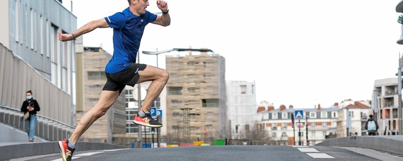 Homme en tee-shirt bleu traversant une route en simulant un saut en course.