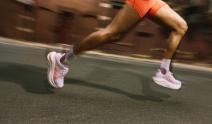 Jambes en mouvement d'une coureuse, qui poste des chaussures HOKA rose pâle à ses pieds.
