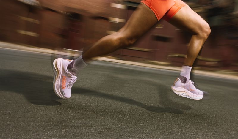 Jambes en mouvement d'une coureuse, qui poste des chaussures HOKA rose pâle à ses pieds.