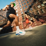 Deux coureurs en mouvement au milieu d'une rue citadine, avec les chaussures HOKA.