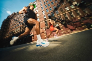 Deux coureurs en mouvement au milieu d'une rue citadine, avec les chaussures HOKA.