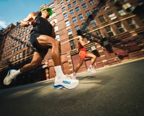 Deux coureurs en mouvement au milieu d'une rue citadine, avec les chaussures HOKA.