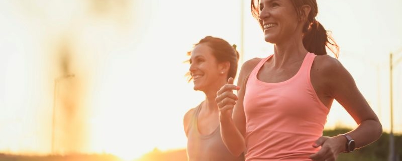 Deux femmes courant au coucher du soleil, sourire aux lèvres.