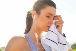 Sportive fatiguée après son entraînement, écouteurs dans les oreilles et serviette posée sur les tempes.
