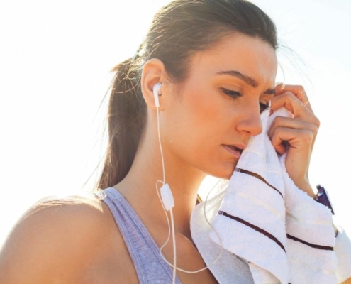 Sportive fatiguée après son entraînement, écouteurs dans les oreilles et serviette posée sur les tempes.