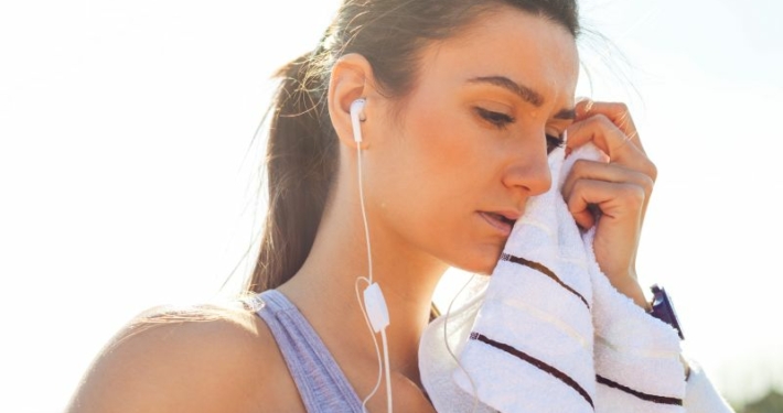 Sportive fatiguée après son entraînement, écouteurs dans les oreilles et serviette posée sur les tempes.
