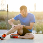 Coureur assis sur le sol, tenant son genou douloureux entre ses mains.