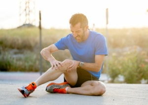 Coureur assis sur le sol, tenant son genou douloureux entre ses mains.