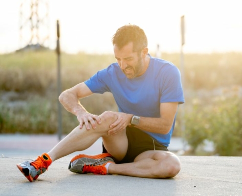 Coureur assis sur le sol, tenant son genou douloureux entre ses mains.