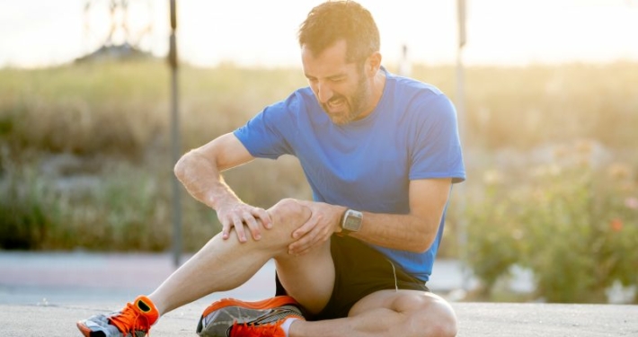 Coureur assis sur le sol, tenant son genou douloureux entre ses mains.