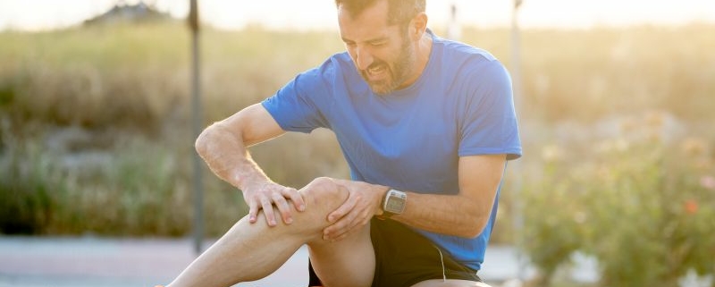 Coureur assis sur le sol, tenant son genou douloureux entre ses mains.