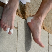 Focus sur des pieds souffrants d'ampoules au niveau du talon et des orteils. Des pansements blancs sont présents à ces endroits.
