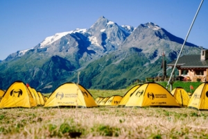 Plusieurs tentes jaunes sur fond de montagnes, pour servir aux participants qui ont choisi l'option bivouac.
