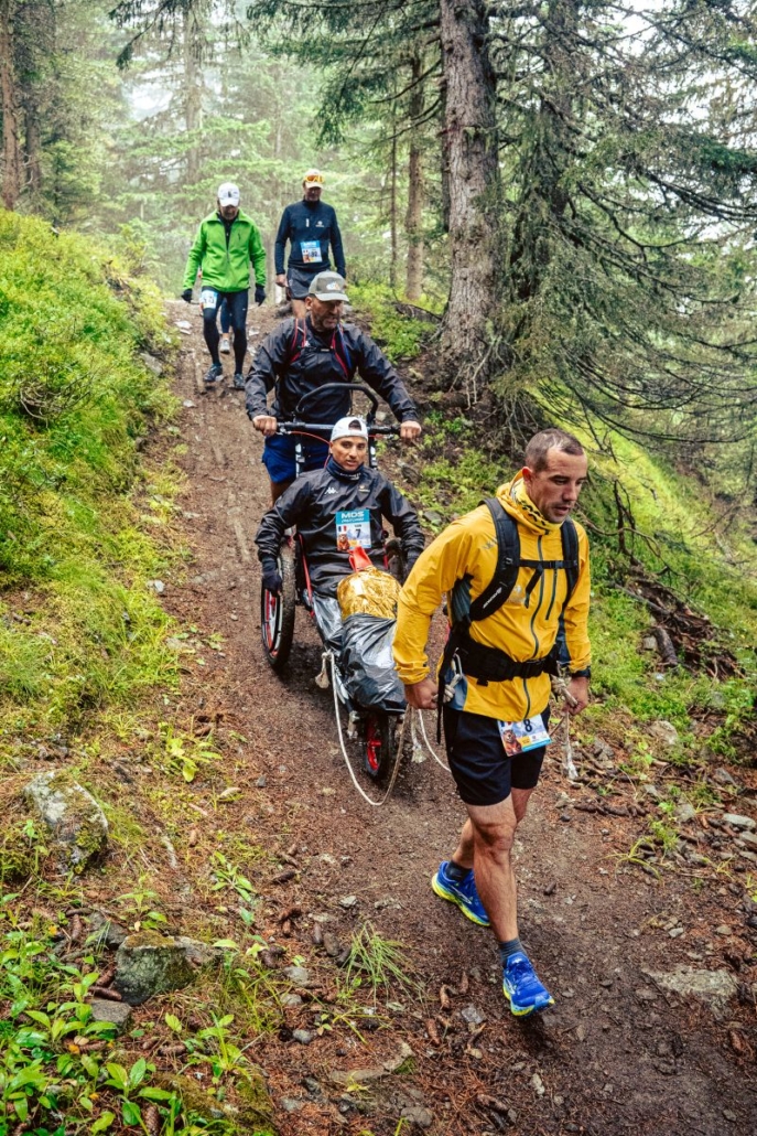 Fauteuil tout-terrain poussé par les Helping Runners lors du MDS Crazy Loops, en descente.