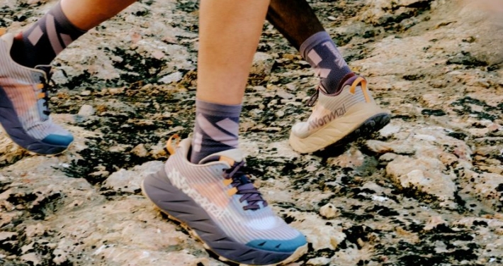Focus sur la paire de NNormal Cadi, en exposition aux pieds de coureurs sur un sol rocheux