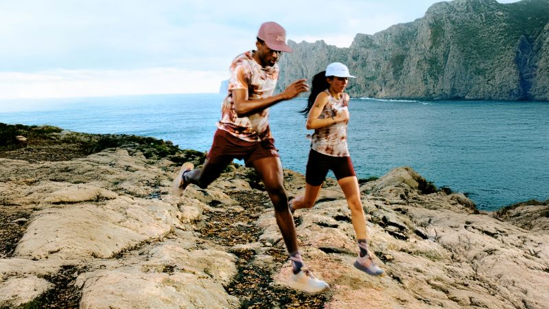 Deux coureurs, un homme et une femme, courant sur un sol rocheux avec en arrière-plan, la mer. Ils portent une paire de NNormal Cadi