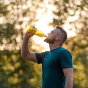 Homme barbu, en tee-shirt bleu, buvant dans une grande bouteille.