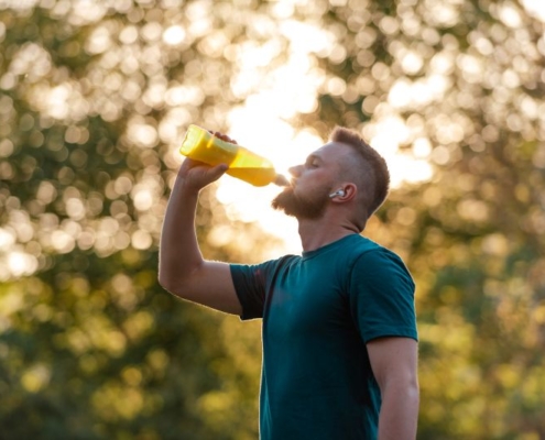 Homme barbu, en tee-shirt bleu, buvant dans une grande bouteille.
