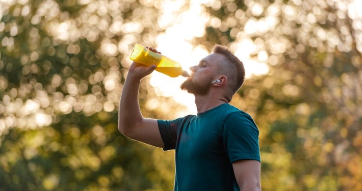 Homme barbu, en tee-shirt bleu, buvant dans une grande bouteille.